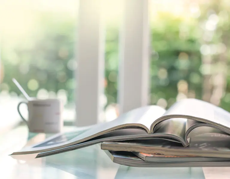 Aufgeschlagenes Magazin auf Tisch mit Kaffeetasse im Hintergrund, stimmungsvolle Szene in hell beleuchtetem Raum, ideal für Inspiration und entspanntes Lesen im modernen Wohnumfeld.